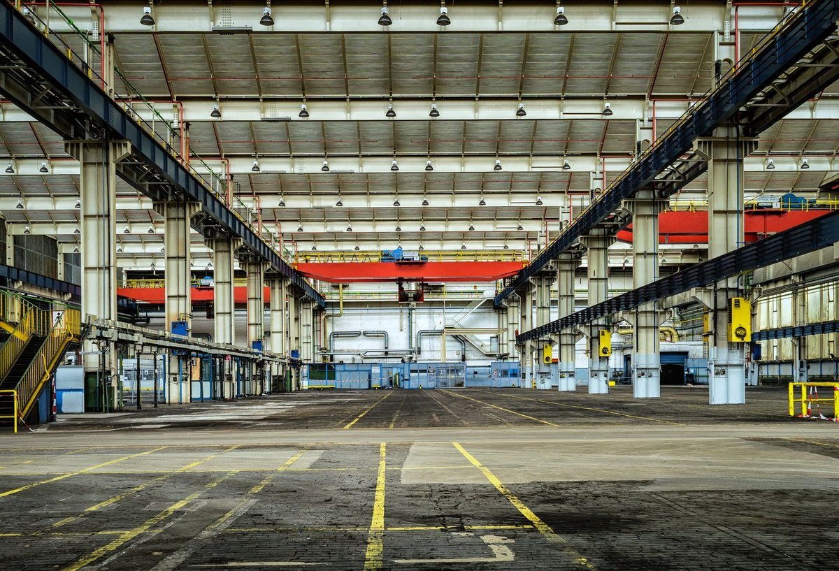 Empty industrial factory floor with yellow safety markings and a red overhead crane